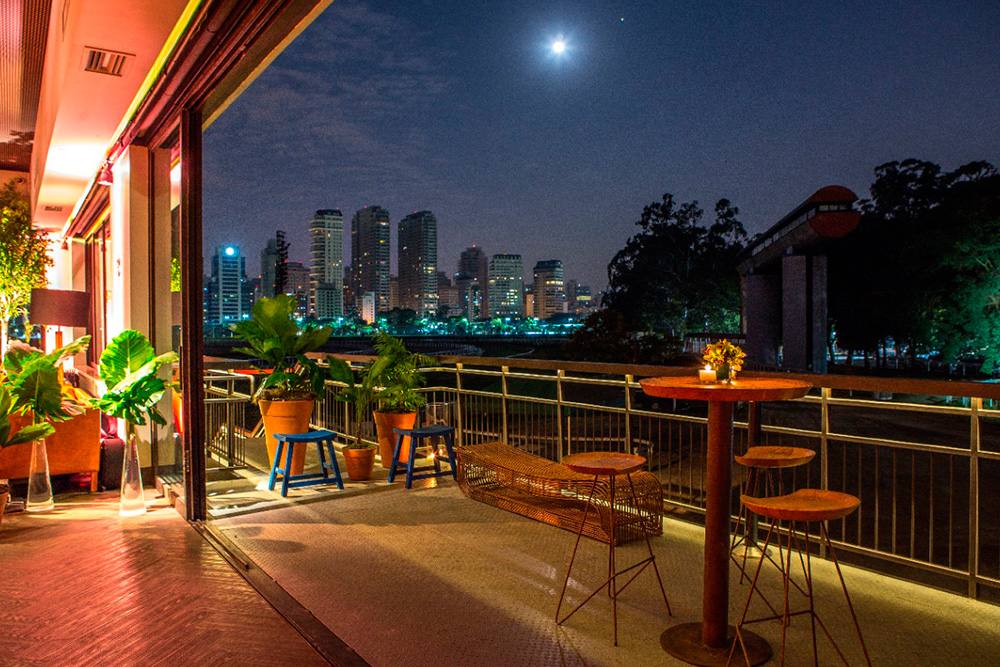 Terraço do Iúlia à noite, com mesas altas e o skyline de São Paulo ao fundo